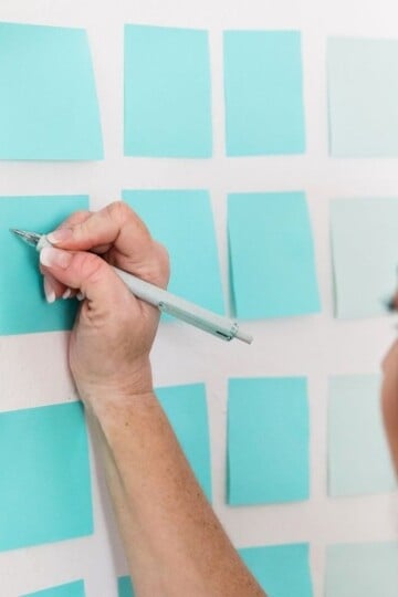 woman working on writing out 12 month savings challenge on blue post it notes on wall