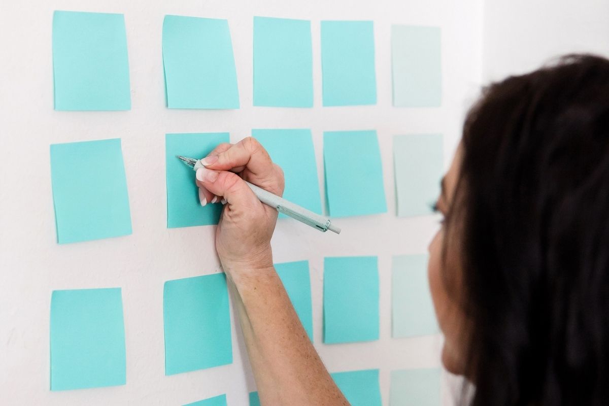 woman working on writing out 12 month savings challenge on blue post it notes on wall