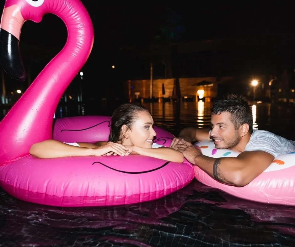 couple in big pink flamingo pool floats, at midnight