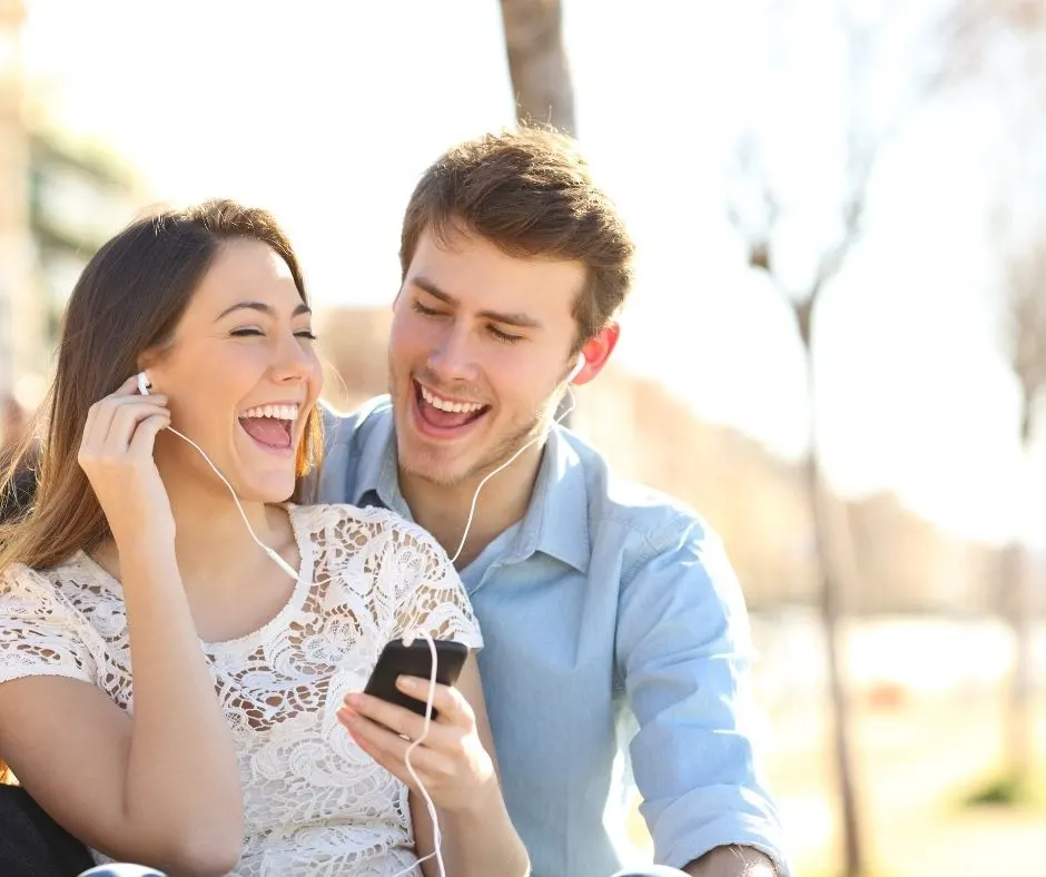 couple sharing earbuds on park bench, listening to crime podcast together