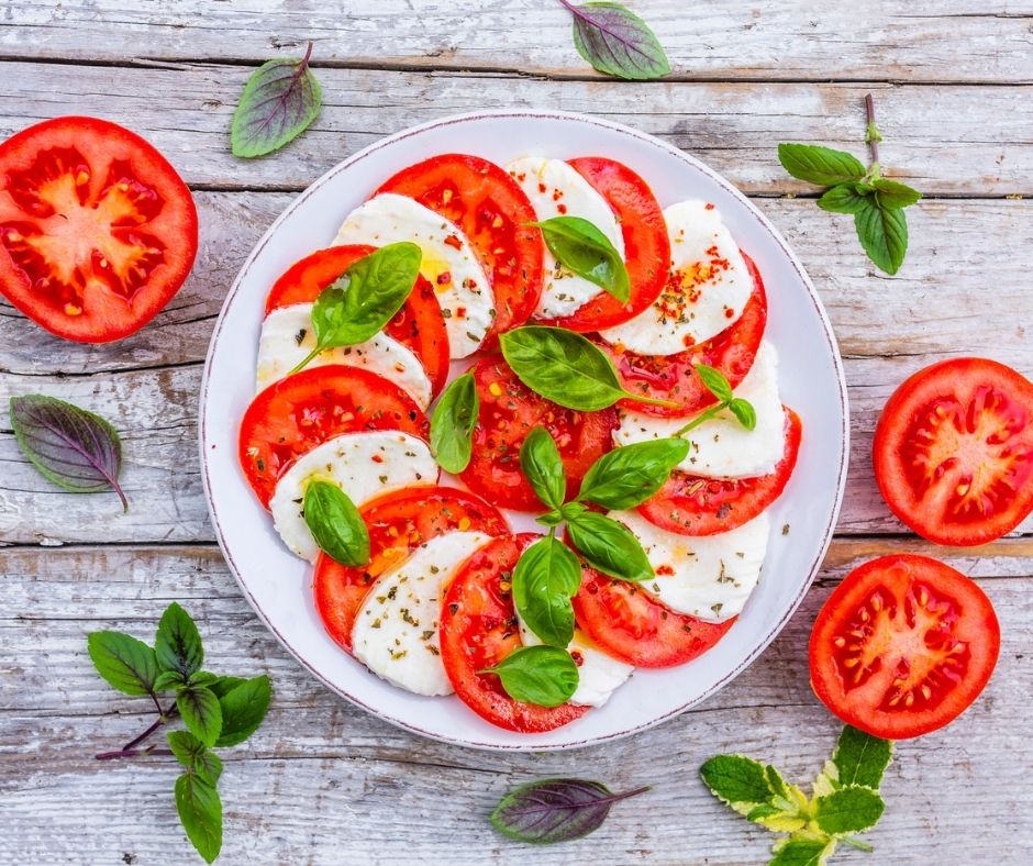 bright caprese tomato, mozzarella, and basil salad with seasonings on white plate on picnic table