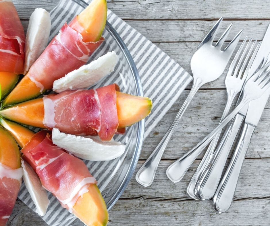 prosciutto wrapped cantaloupe wedges on glass plate on picnic table