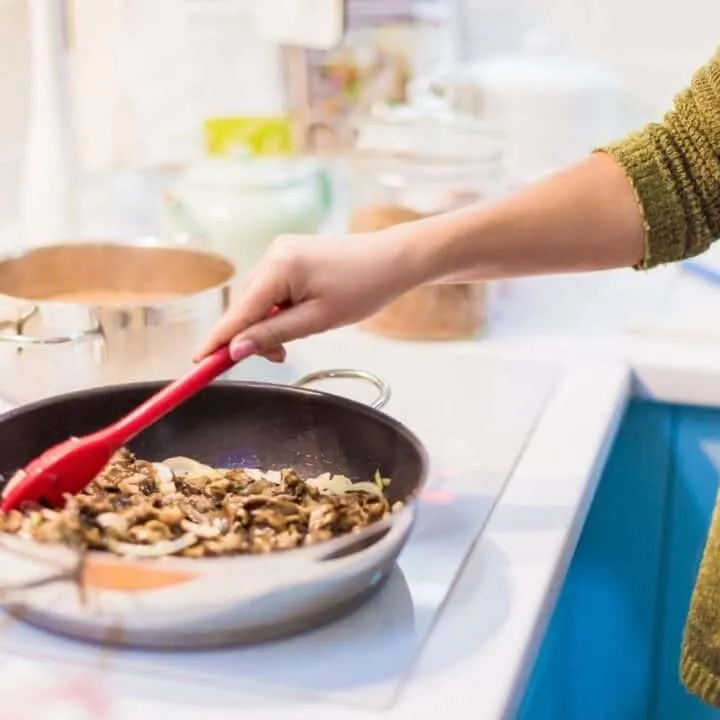 woman standing at stovetop, cooking with a red spatula