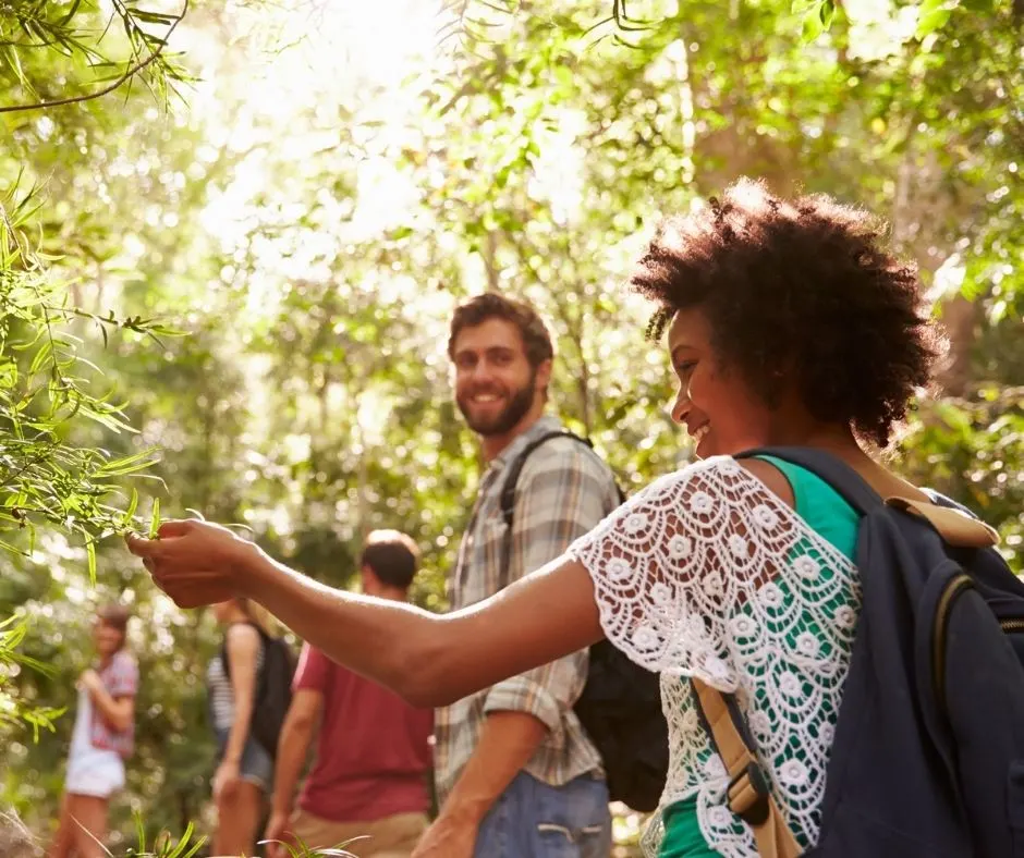 group of adults hiking, with woman touching green leaves and smiling