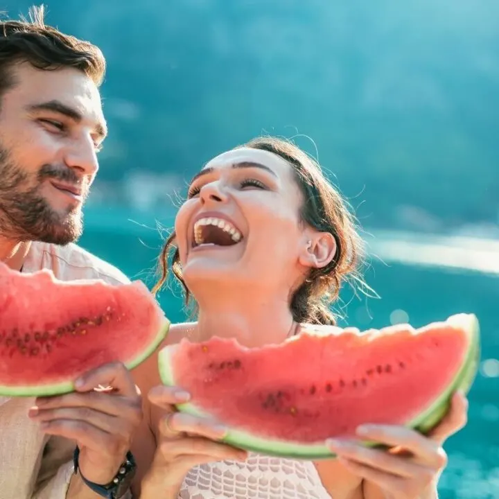 young couple eating watermelon outside, laughing