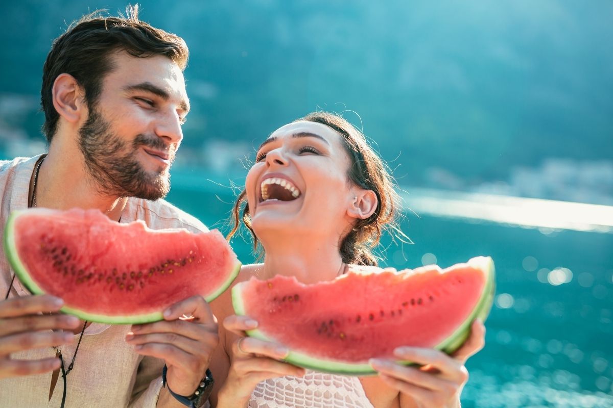 young couple eating watermelon outside, laughing