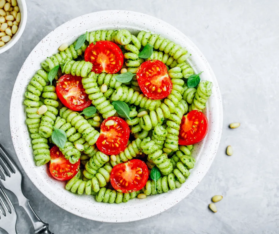 white dish of pesto pasta salad with tomatoes