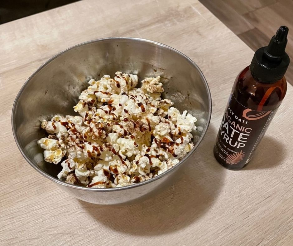metal bowl of chai popcorn drizzled with Just dates date syrup bottle on right