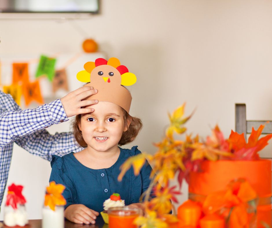 young girl getting chosen as Honorary Thanksgiving guest, boy putting turkey decoration on her head