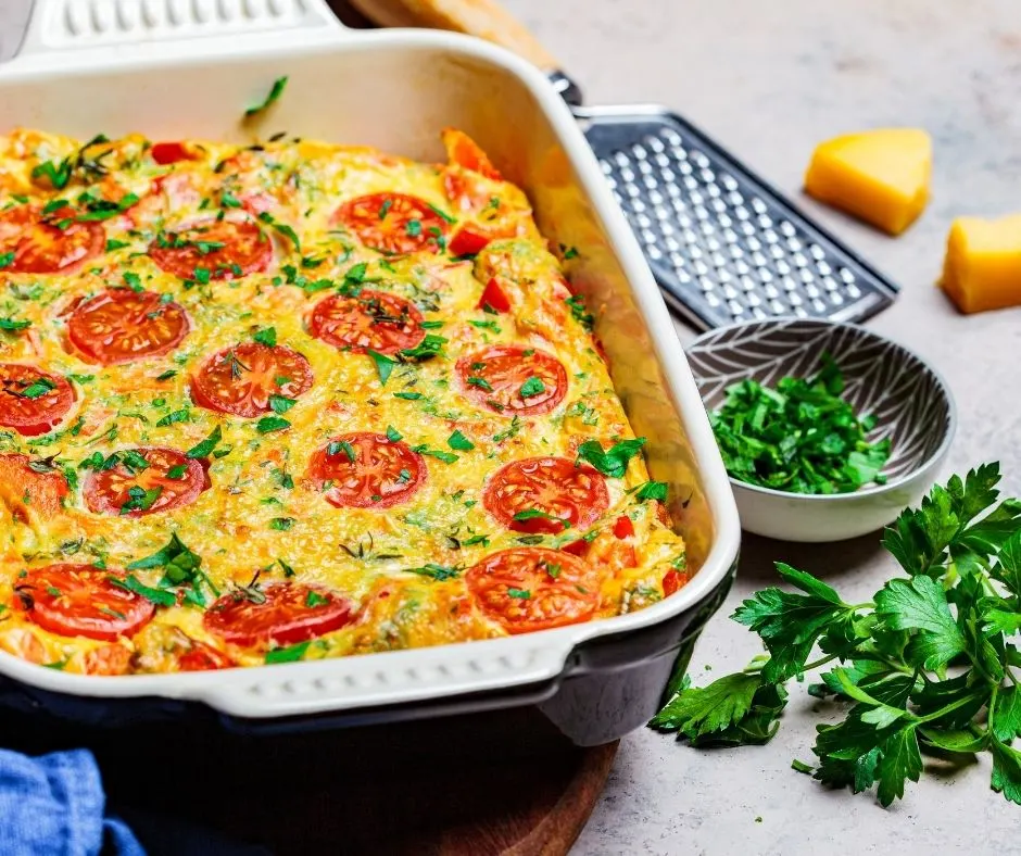 make ahead frittata with spinach and tomatoes on table with cheese grater and herbs