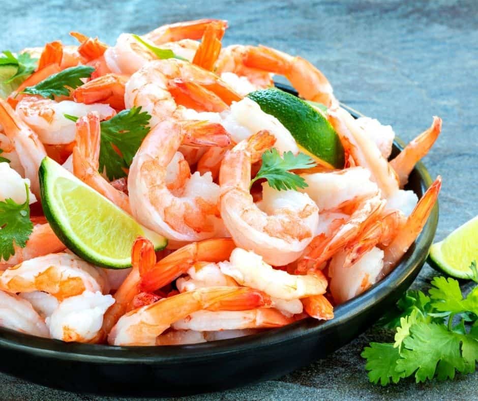 shrimp cocktail in large black bowl, with limes and cilantro