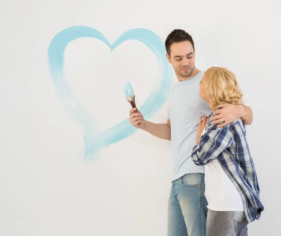 couple in jeans and comfy clothes, painting blue heart on wall