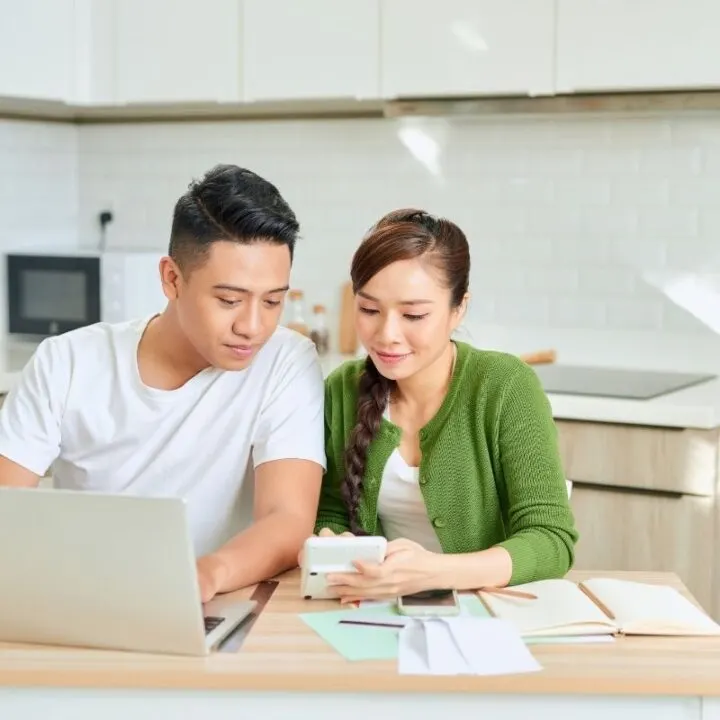 young couple at laptop and kitchen table, working with free family budgeting tools