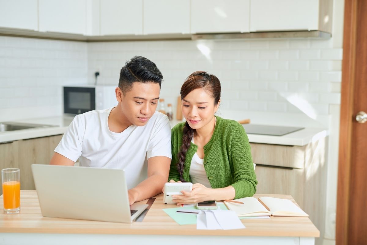 young couple at laptop and kitchen table, working with free family budgeting tools