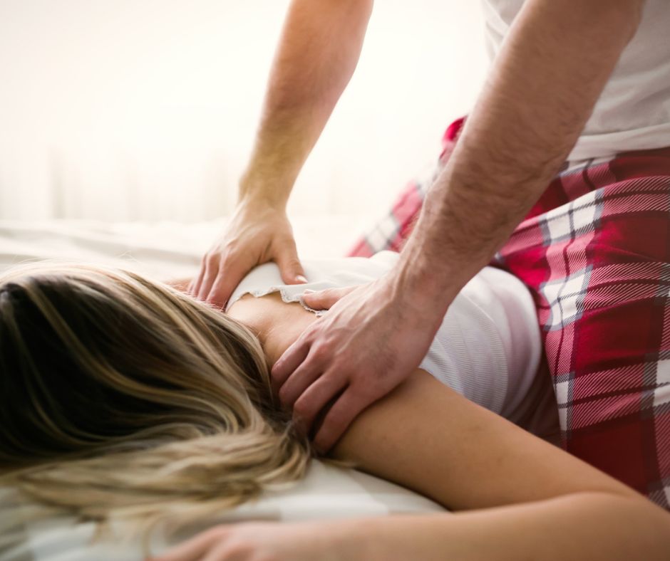 husband in red flannel pants massaging wife's back in bed