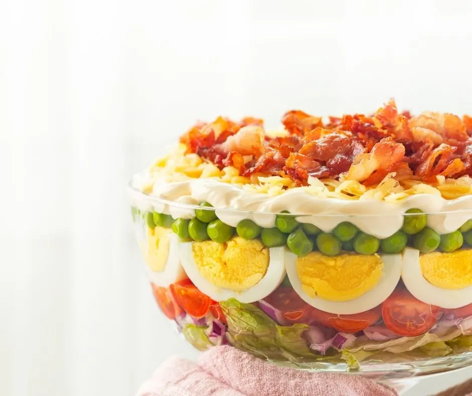 clear bowl showing different layers of make ahead summer salad for groups