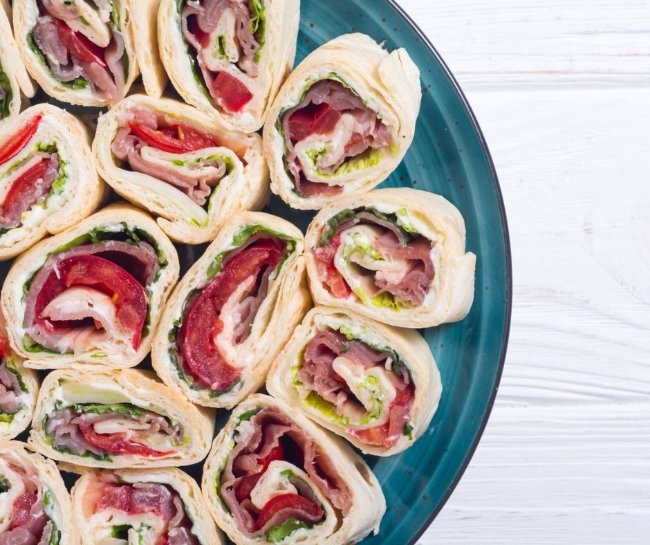 blue platter of turkey roll up sandwiches with tomatoes, greens, and sauce