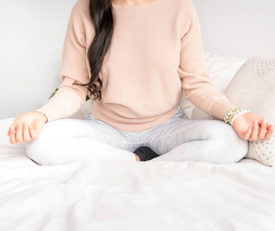 woman in pink shirt and jogger pants in bed, meditating