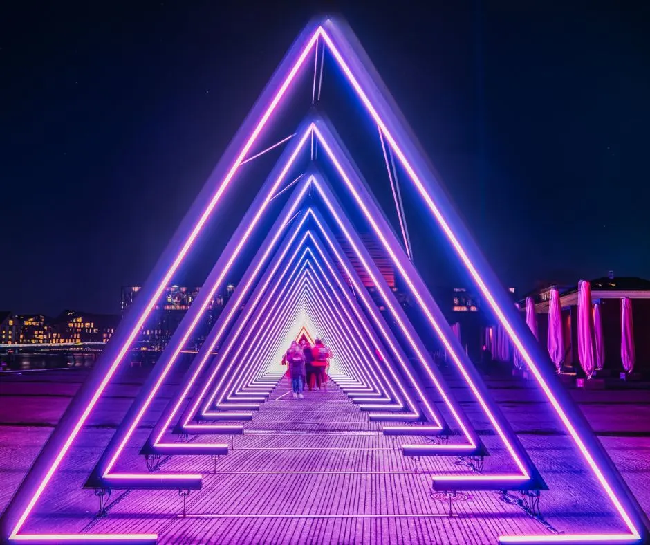 neon blue and purple huge triangle people are walking through on autumn night