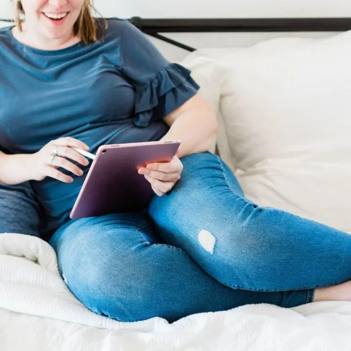 woman in jeans on couch, smiling and using iPad to find frugal tips