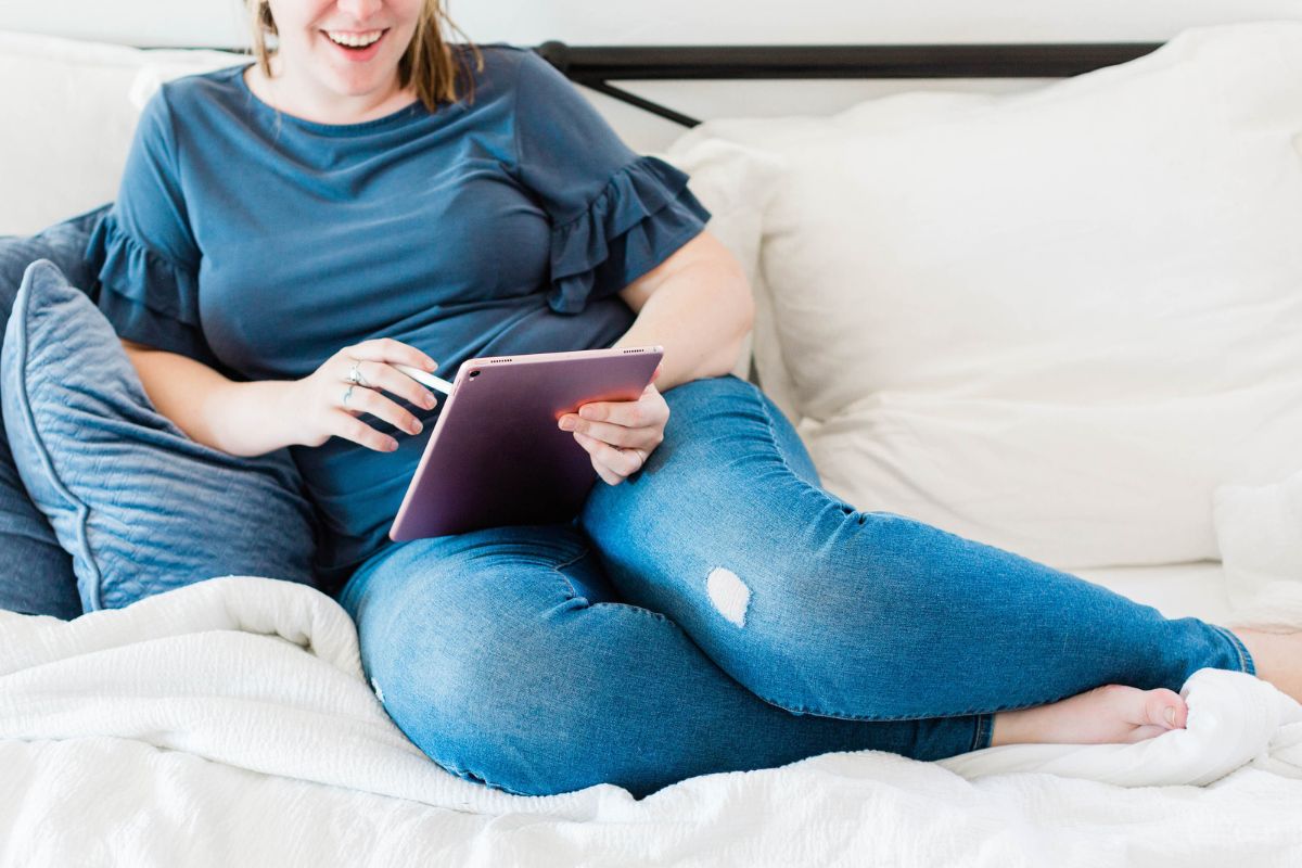woman in jeans on couch, smiling and using iPad to find frugal tips