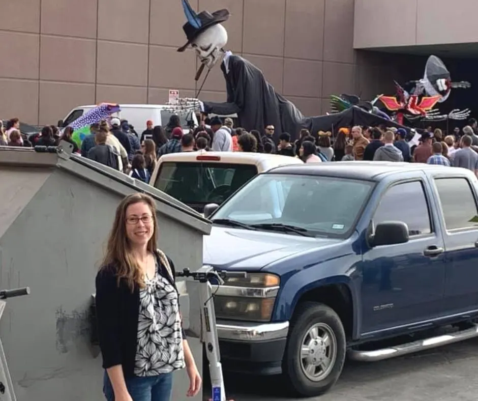 author standing in front of Day of the Dead parade with large skeletons