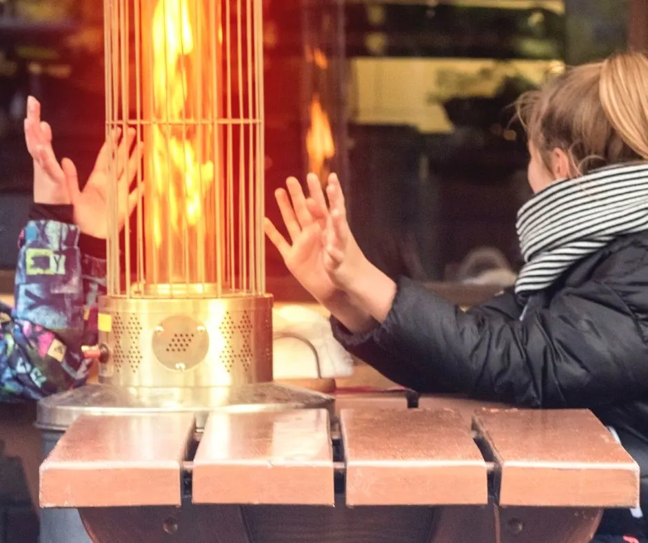 two ladies on restaurant patio, bundled up, enjoying time outdoors next to fire heater