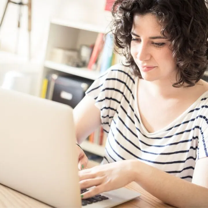 woman with curly black hair in striped shirt on laptop smiling at frugal year challenges
