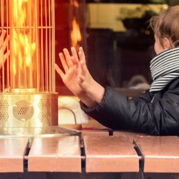 two women at restaurant on patio bundled up, warming hands by patio fire