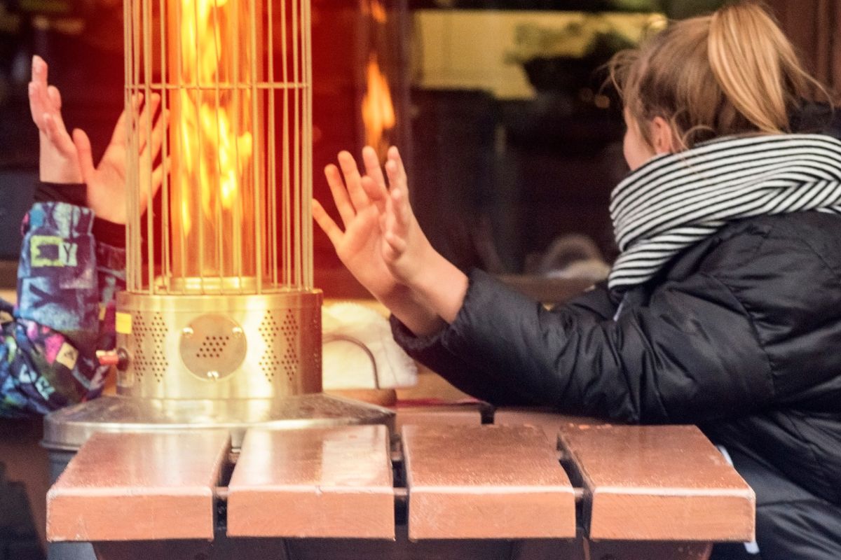 two women at restaurant on patio bundled up, warming hands by patio fire