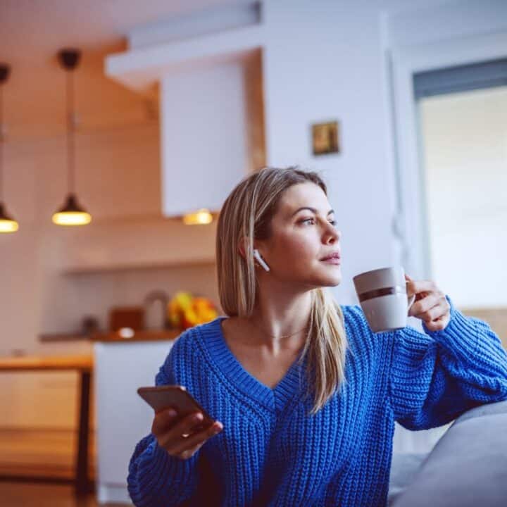 woman in blue sweater with coffee on couch listening to horror audiobook