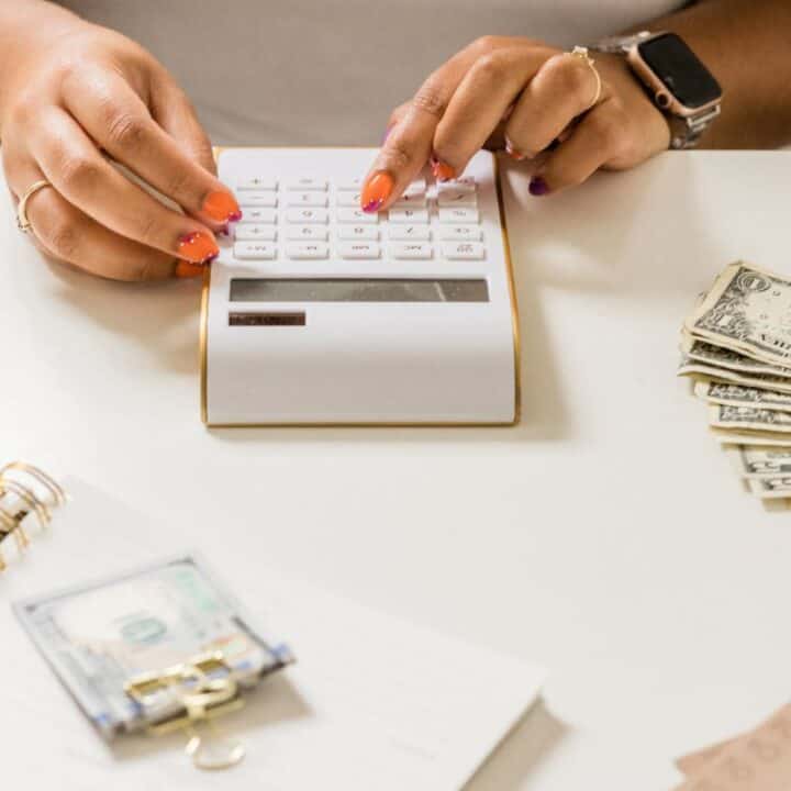 woman with orange nails using calculator to budget her cash at desk