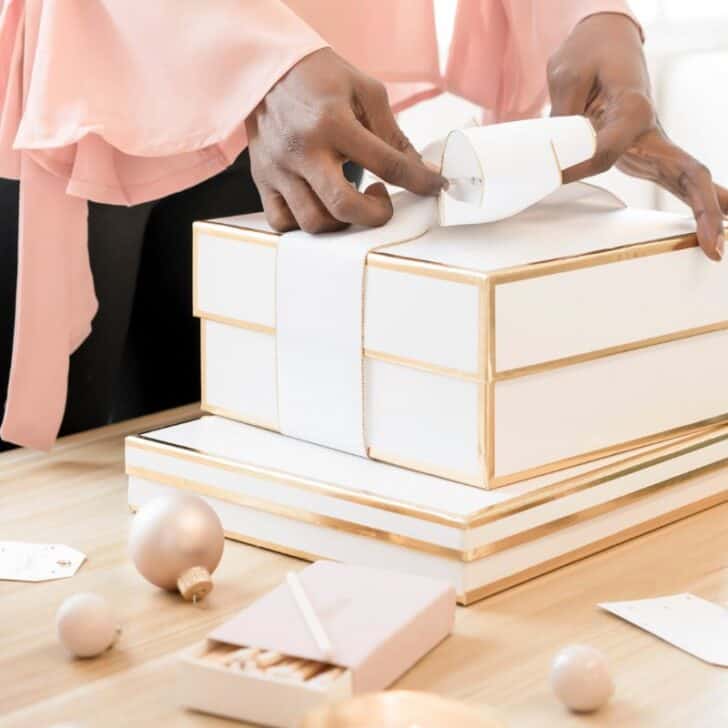 woman wrapping gifts in white, chic wrapping, next to her Christmas list organizer