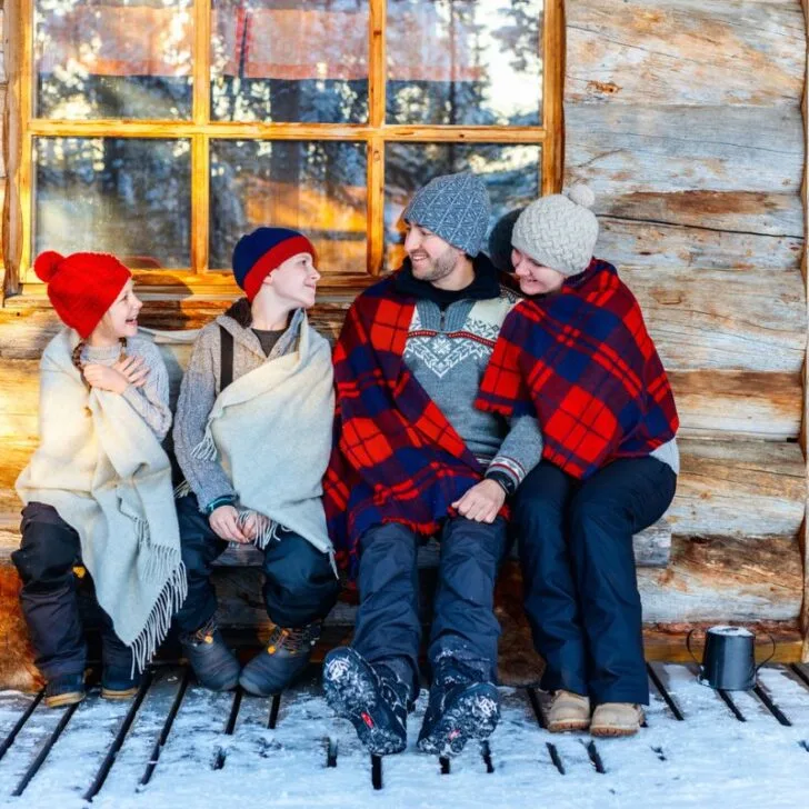 family in plaid blankets on porch of cottage on family winter staycation