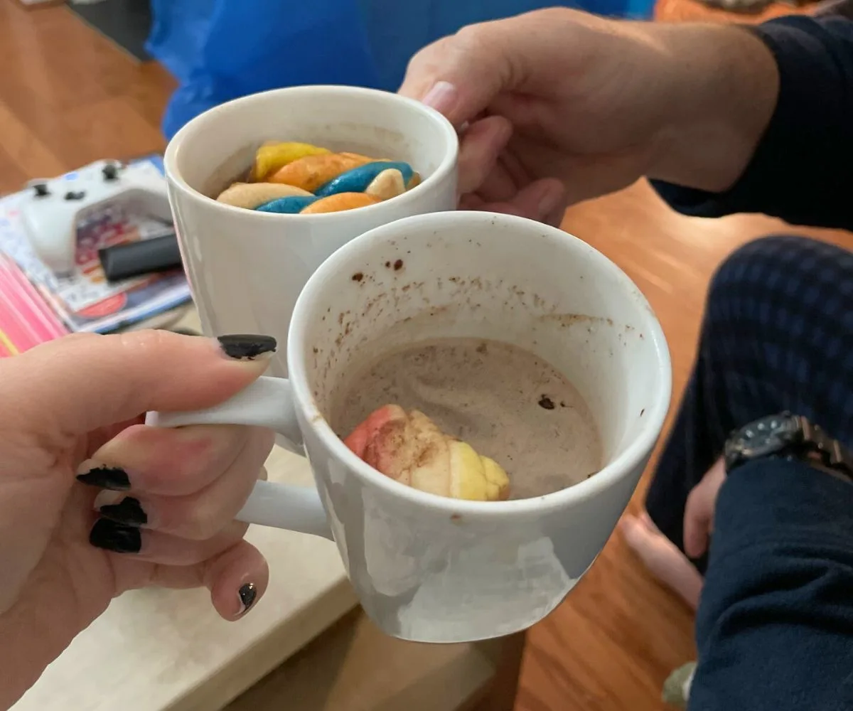 couple doing a cheers with hot cocoa mugs and unicorn marshmallows floating in them