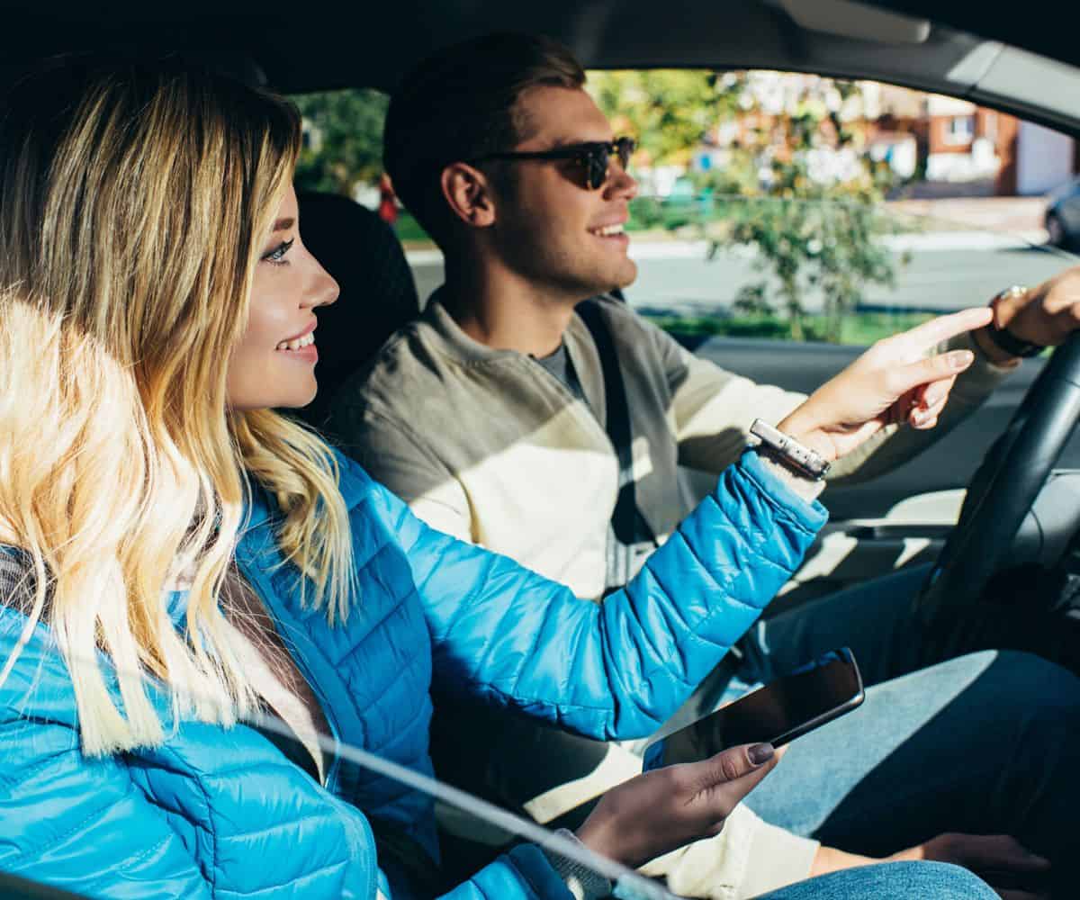 man and woman driving to Dollar Store, woman pointing out the window and smiling