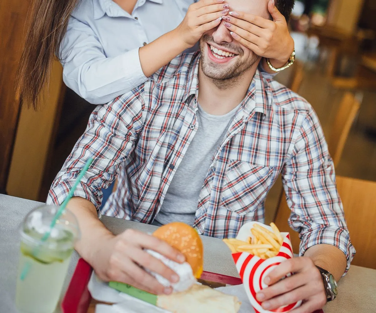 woman putting hands around man's eyes to surprise him with dollar menu items
