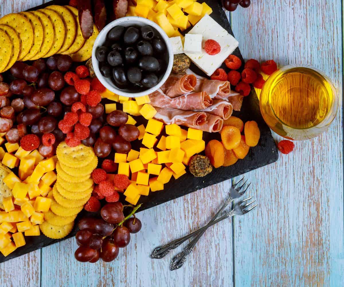 board of fruit, cheeses, crackers, and honey on blue table
