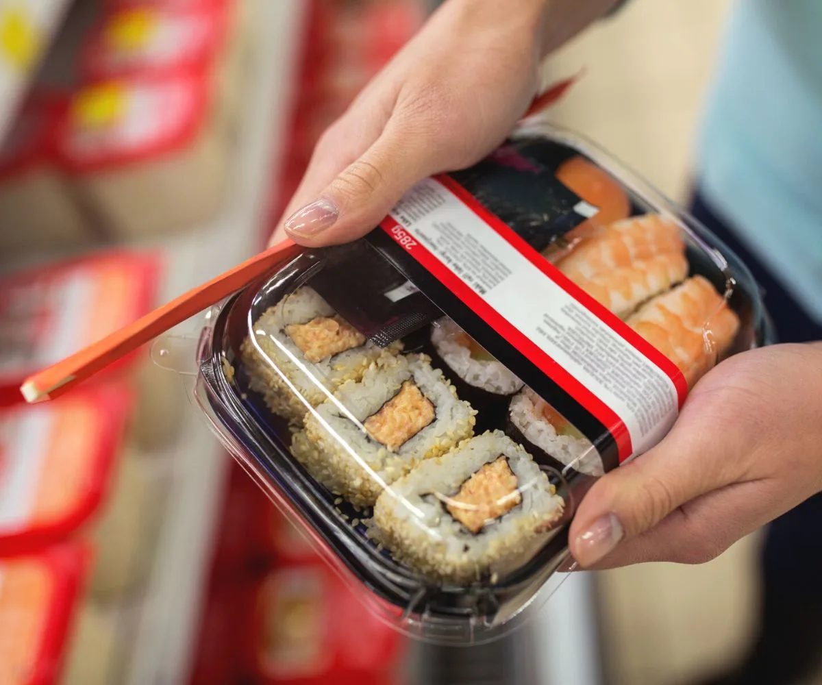 woman holding box of grocery store sushi with chopsticks