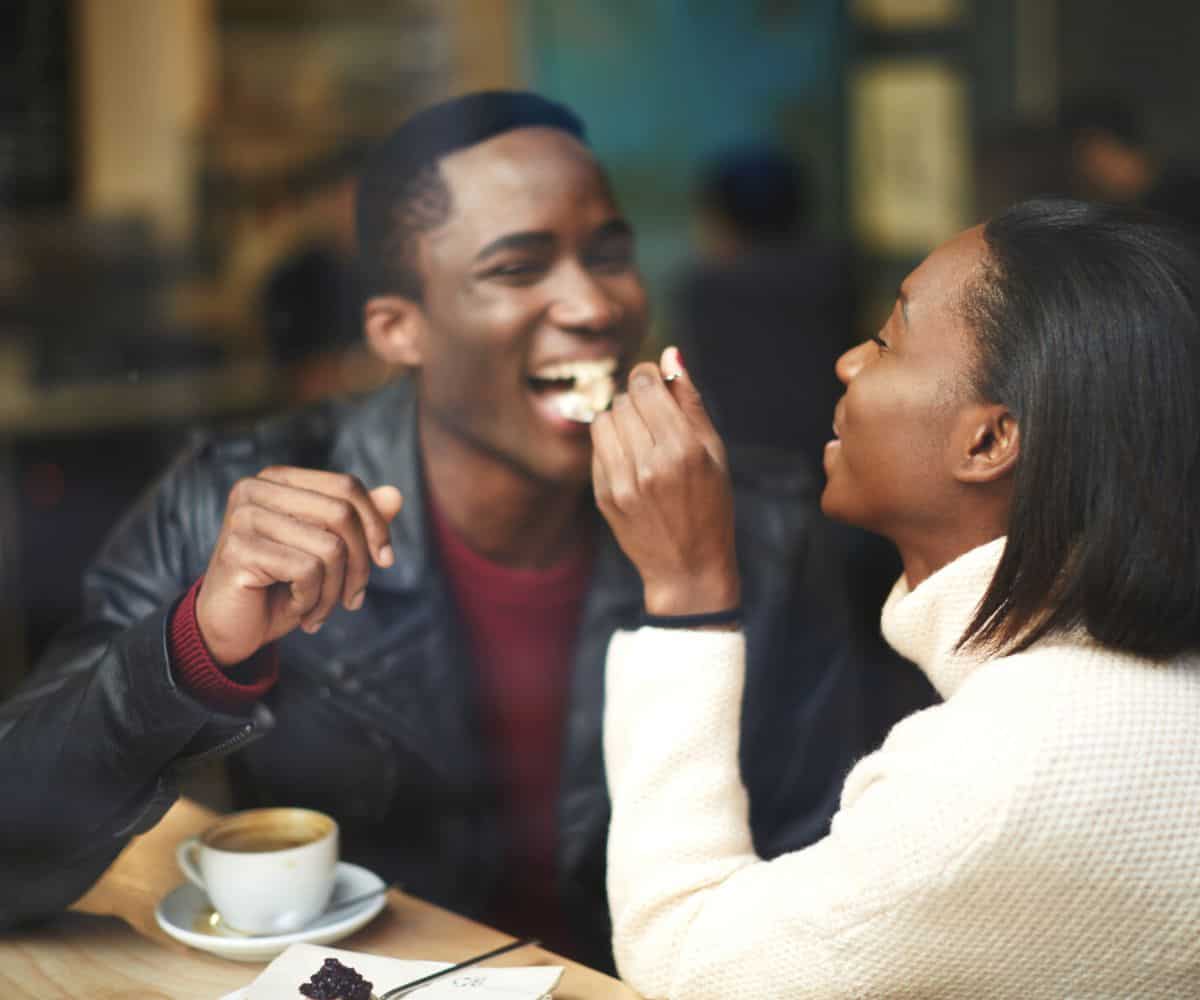 woman feeding man cake at coffee shop, laughing