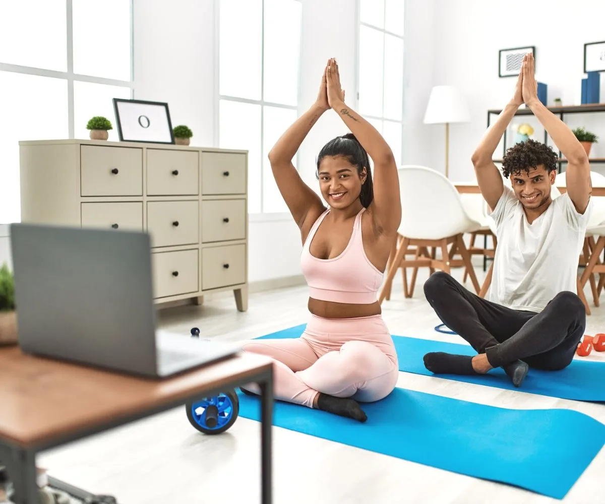 couple smiling, doing yoga on laptop at home