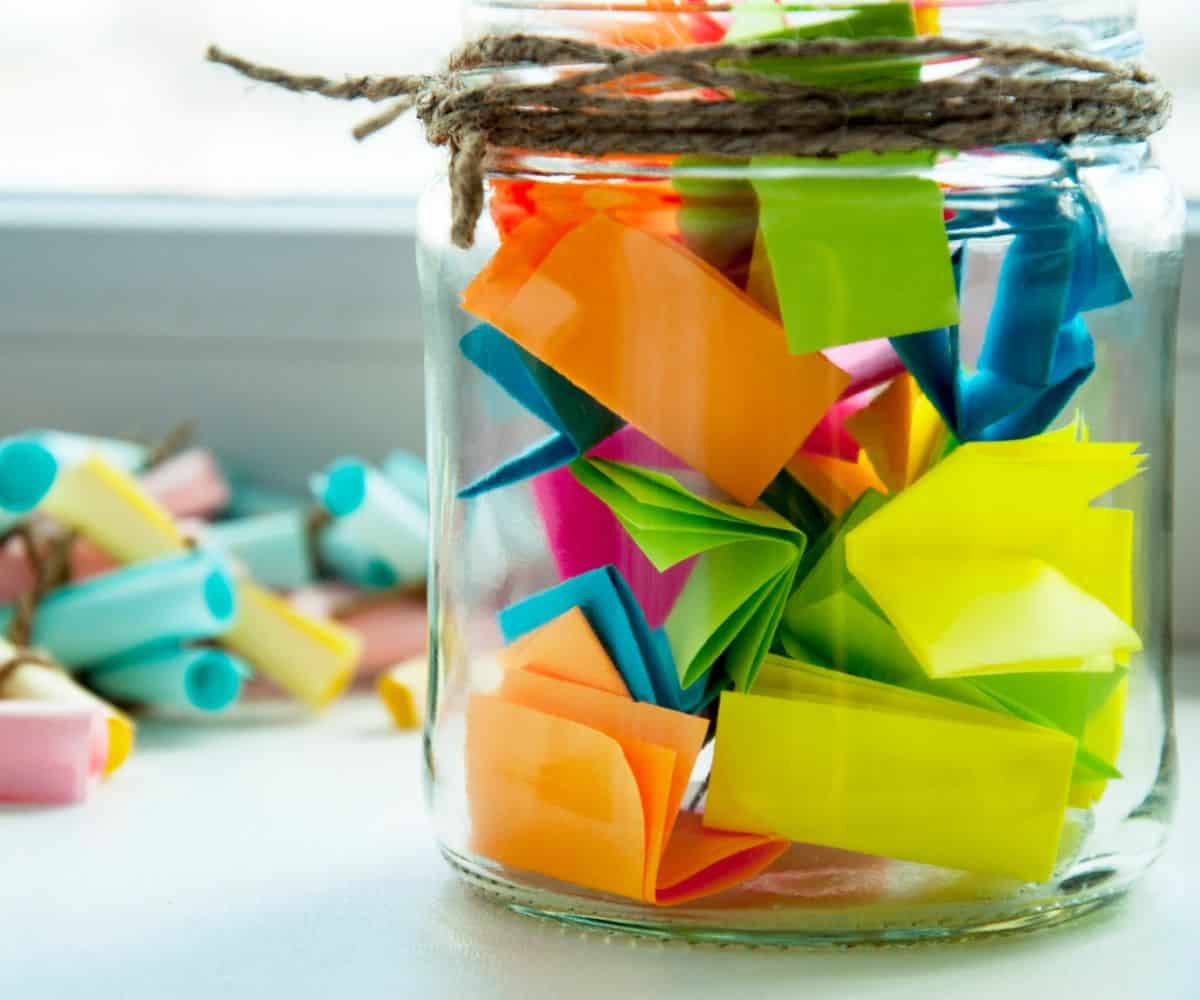mason jar with twine filled with brightly colored folded pieces of paper