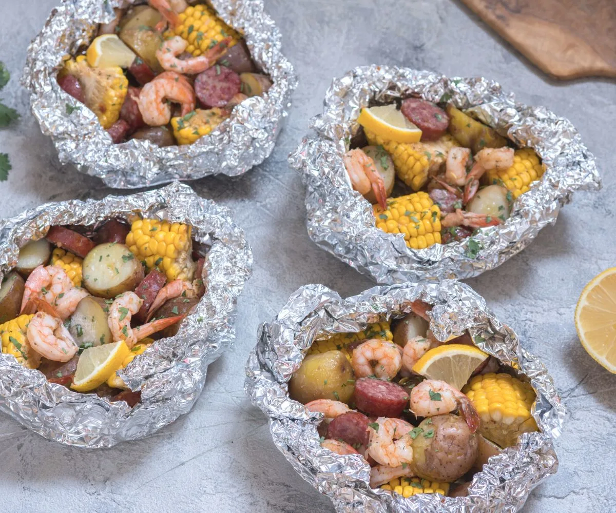 four foil pack dinners of shrimp, sausage, corn, and lemons