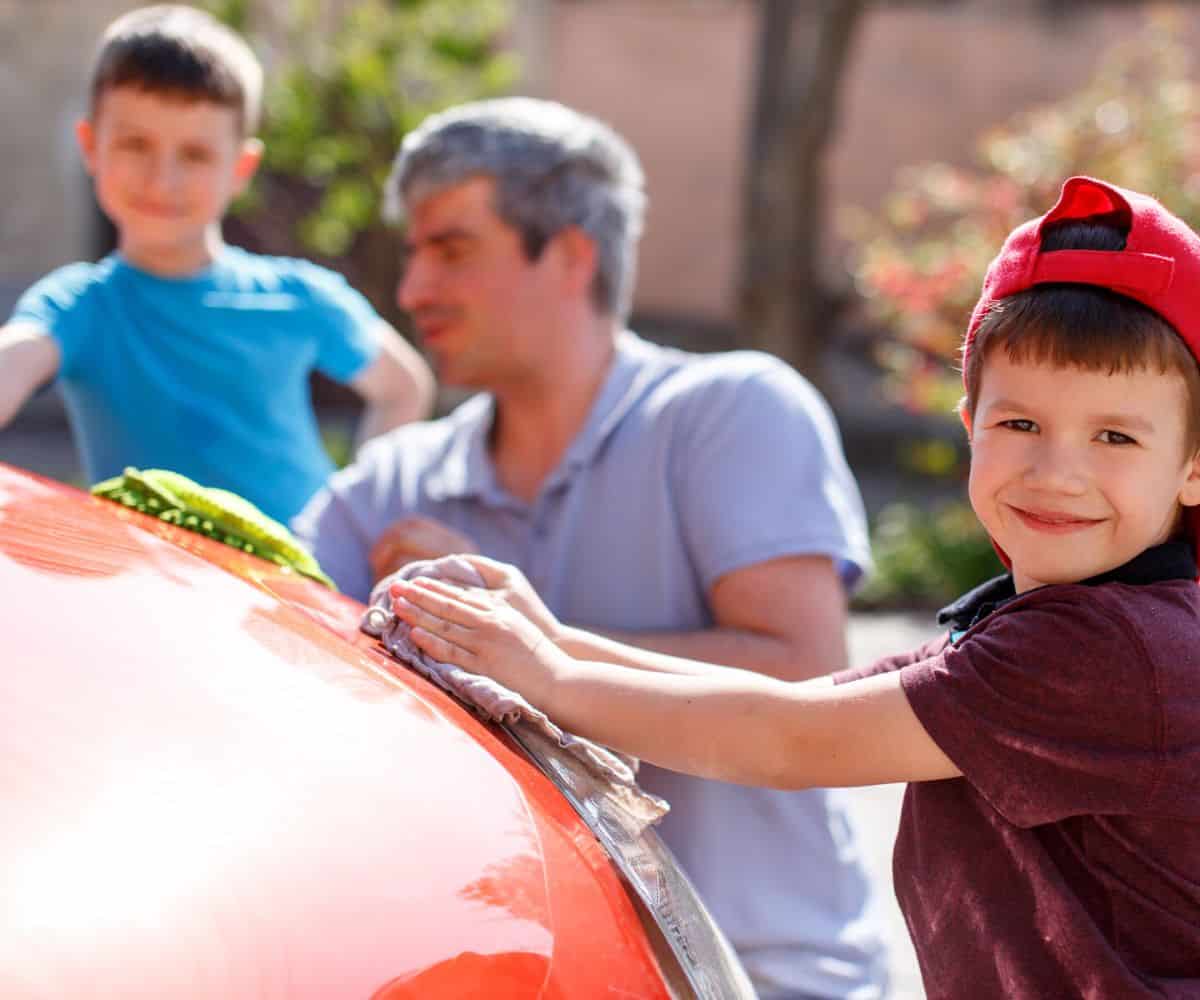 husband with two young kids cleaning wife's red car