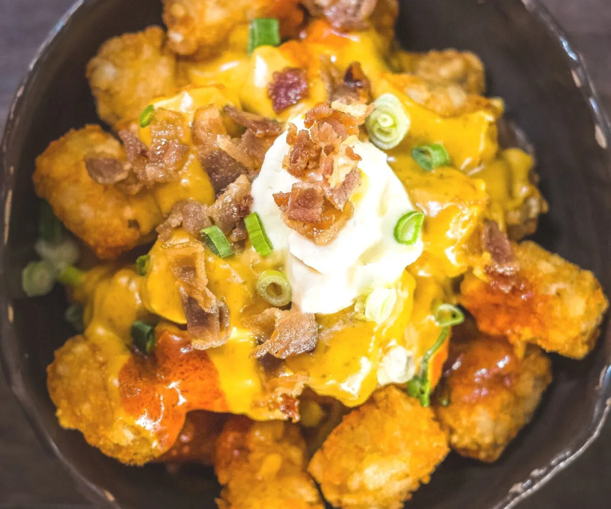 bowl of tator tot totchos with cheese, enchilada sauce, and sour cream on top