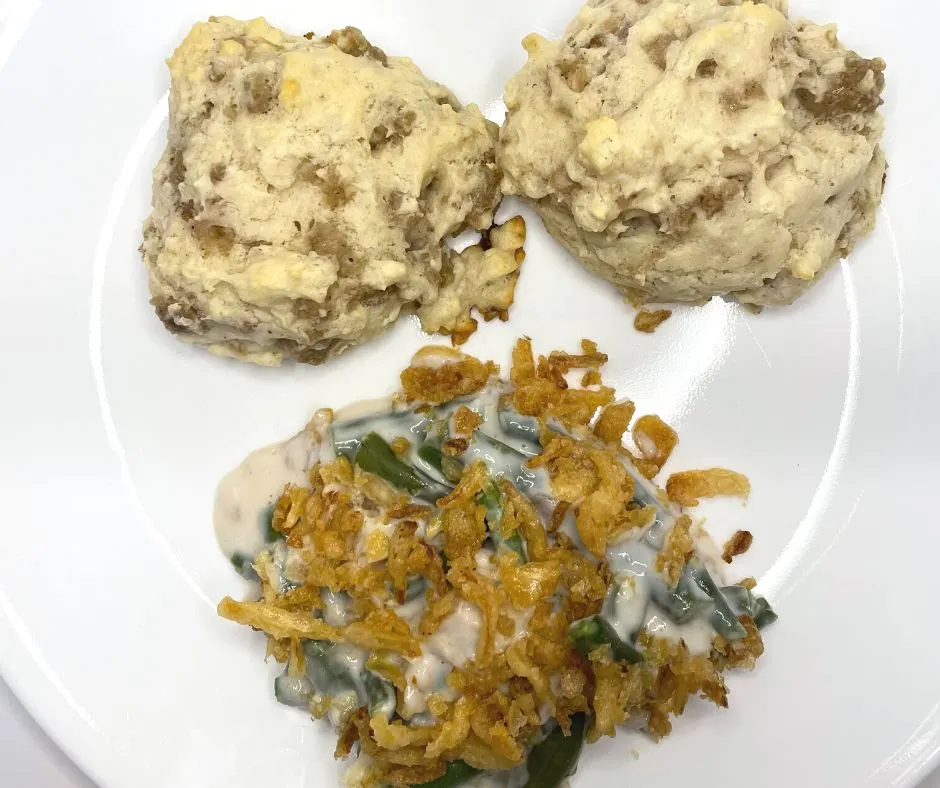 white plate with two sausage biscuits and pile of green bean casserole with crispy fried onions