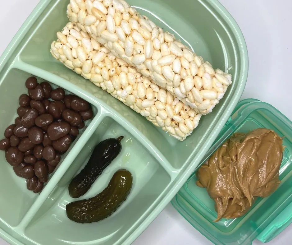 two rice sticks, chocolate raisins, two sweet pickles, and small container of peanut butter