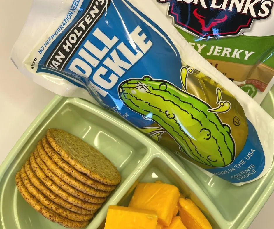 giant dill pickle, beef jerky, crackers, and cheddar cheese in 3-compartment dollar tree lunch container