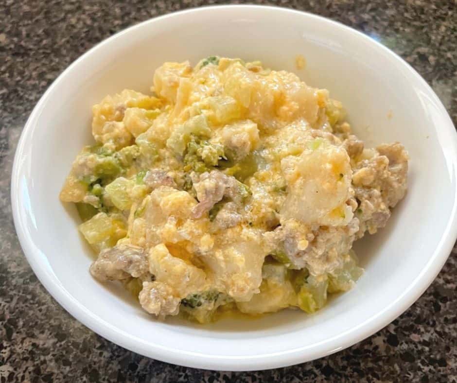 white bowl in dark countertop with cheesy sauce, potatoes, broccoli, and sausage