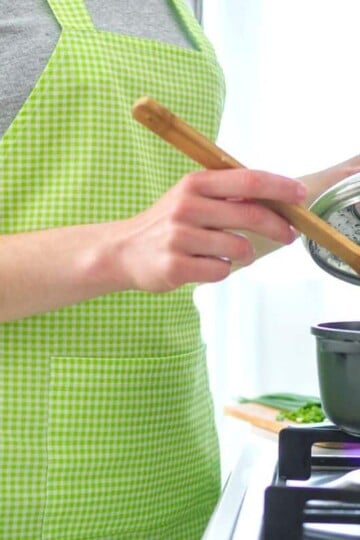 woman in light green apron stirring dollar tree dinner in a pot on stove